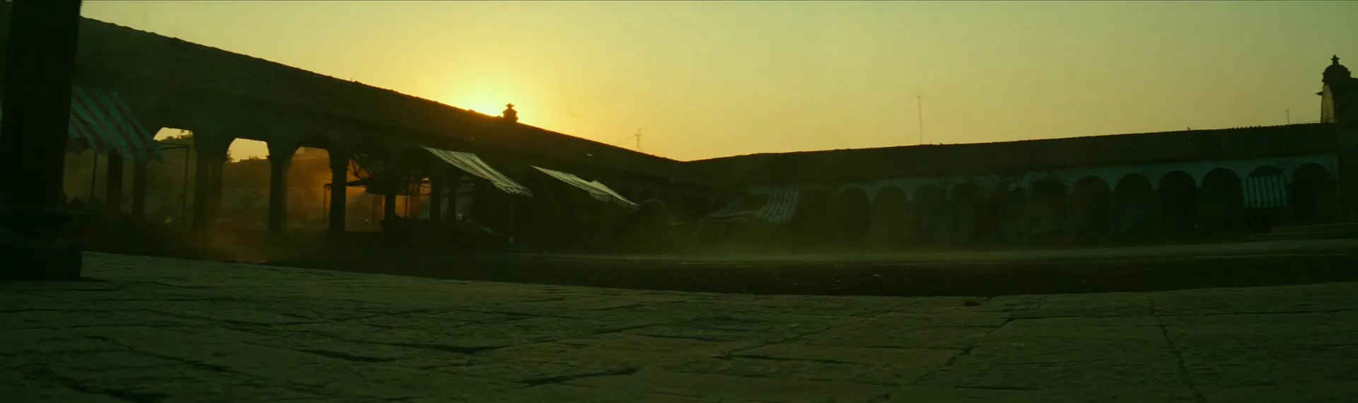 Row of market stalls under striped awnings at dawn, silhouetted against the rising sun